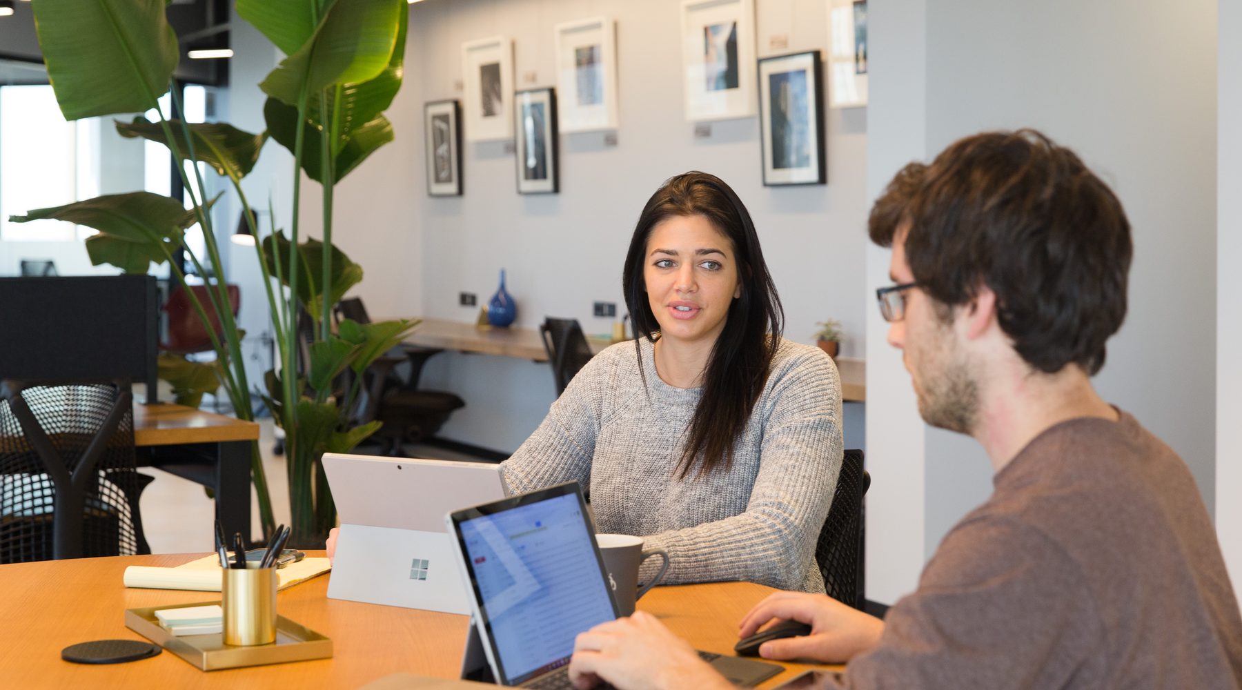 A man and woman collaborating on tablet computers at a wooden table in a Charlotte coworking office used by Atlas AI consulting