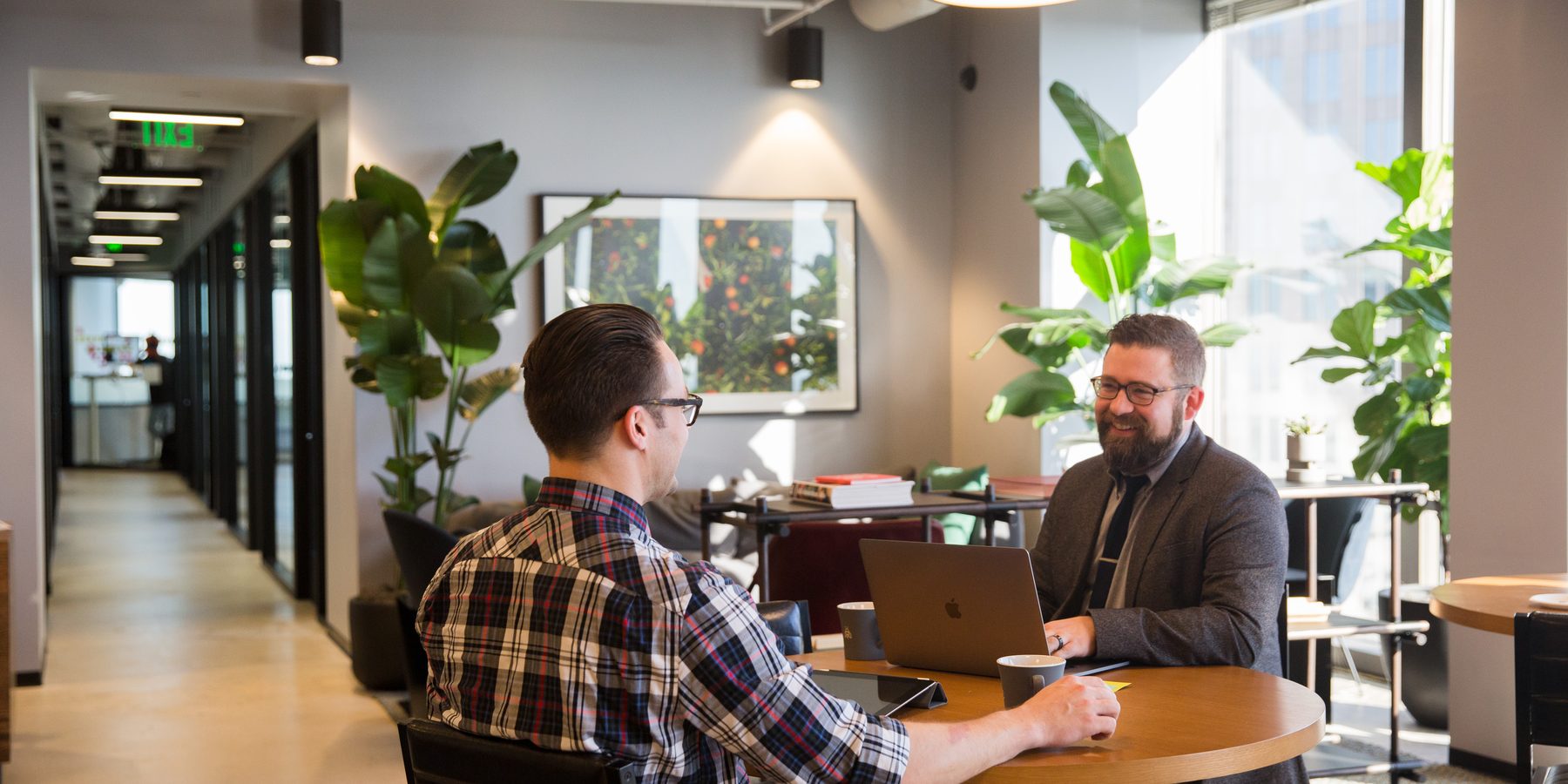 Two professionals reviewing work on a MacBook and tablet at a round table in a Charlotte coworking space during an Atlas AI consulting session